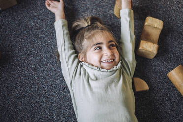 Directly above view of happy girl lying down with arms raised in classroom - MASF43074