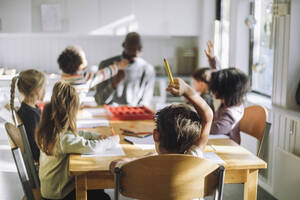 Boy raising hand while sitting in classroom during Q and A session at kindergarten - MASF43080