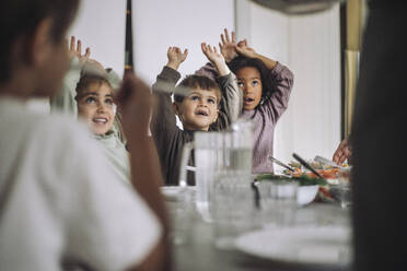 Happy children with arms raised during lunch time at kindergarten - MASF43088