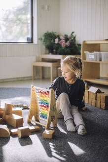 Girl learning to count through abacus while sitting in classroom at kindergarten - MASF43100