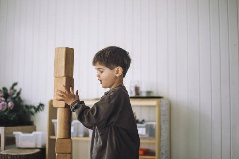 Side view of boy stacking toy blocks while playing in classroom at kindergarten - MASF43101