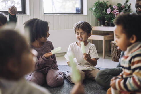 Boy and girl holding popsicle stick while sitting in classroom at kindergarten - MASF43103