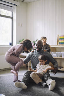 Playful kids having fun with male teacher sitting in classroom at kindergarten - MASF43109
