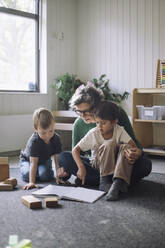 Boys sitting with female teacher reading book in classroom at kindergarten - MASF43113