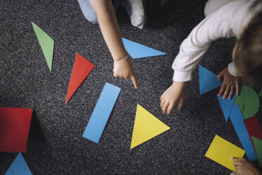 Directly above view of kids playing with geometric shapes on floor in classroom at kindergarten - MASF43115
