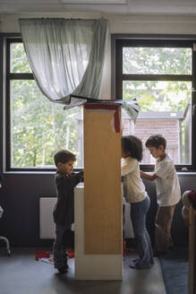Side view of preschool kids playing together near booth in classroom at kindergarten - MASF43120