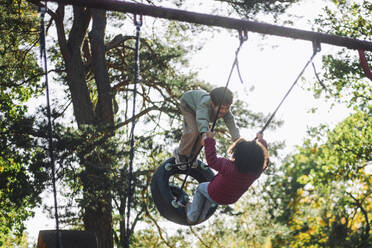 Cheerful boy and girl having fun while swinging at park - MASF43126