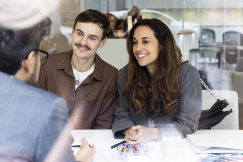 Happy couple meeting with real estate agent at desk in office - MASF43142