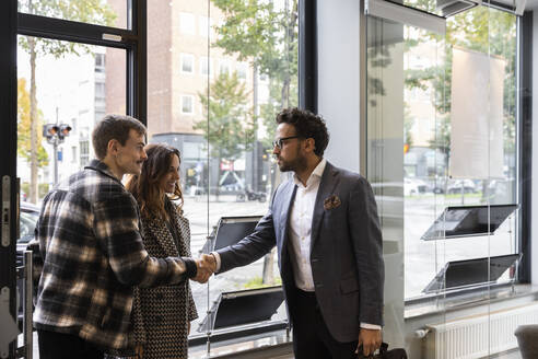 Happy couple shaking hand with real estate agent at entrance of office - MASF43148