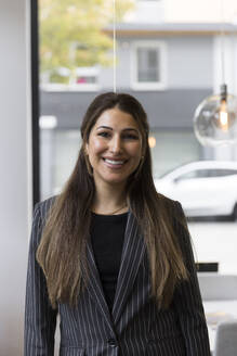 Portrait of smiling female real estate agent wearing blazer standing in office - MASF43149