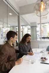 Smiling man looking at woman signing agreement at desk in real estate office - MASF43153