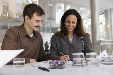 Man looking at smiling woman signing agreement at desk in real estate office - MASF43154