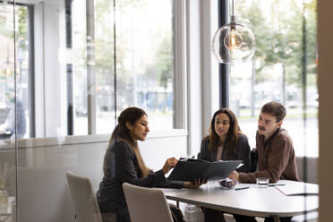 Female real estate agent showing floor plan to young customers while sitting at desk in office - MASF43156