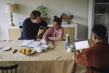 High angle view of gay couple sitting with daughter doing homework while sitting at dining table - MASF43162
