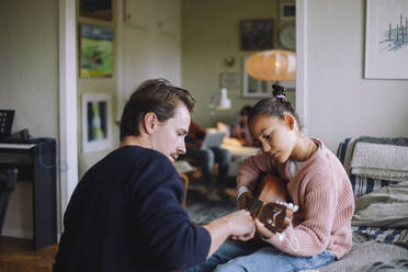 Father teaching daughter to play guitar while sitting on bed at home - MASF43165