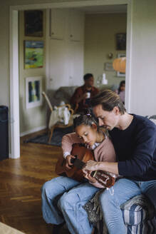 Father sitting with daughter playing guitar in bedroom at home - MASF43167