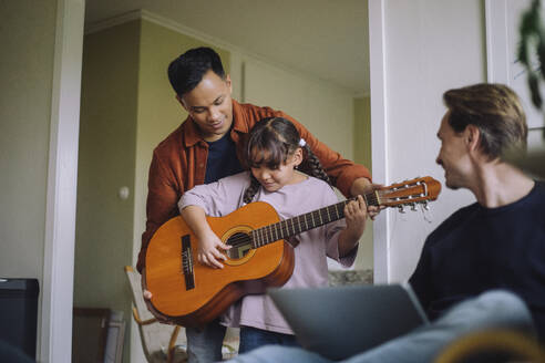 Gay father standing with daughter playing guitar at home - MASF43169