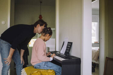 Father assisting daughter playing piano at home - MASF43170