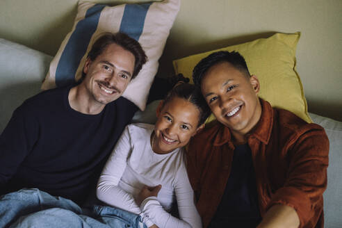 Directly above portrait of gay couple reclining with daughter on sofa at home - MASF43175