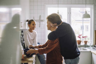 Gay couple talking with daughter while preparing food in kitchen at home - MASF43189