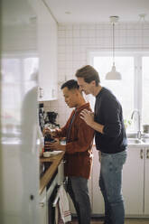 Side view of gay man with hand on shoulder of boyfriend preparing food in kitchen at home - MASF43200