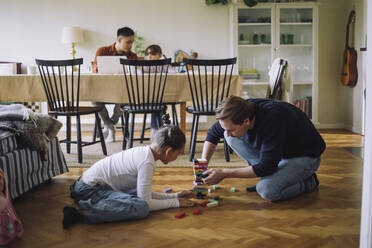 Father teaching daughter to play Jenga while sitting on floor at home - MASF43203