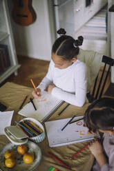 High angle view of female siblings drawing on book while sitting at home - MASF43214