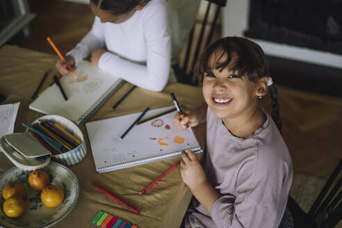 High angle portrait of happy girl coloring while sitting at dining table with sister at home - MASF43215