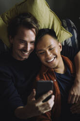 High angle view of smiling gay couple using smart phone at home - MASF43220