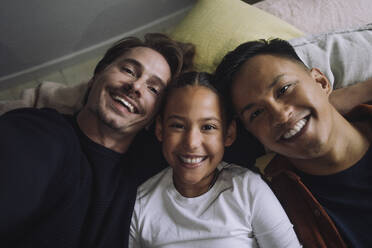 Directly above portrait of smiling gay couple lying down with daughter at home - MASF43223