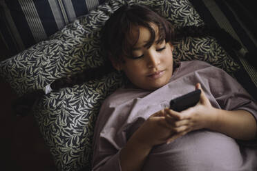 Little girl in underwear lying on bed looking at smartphone stock