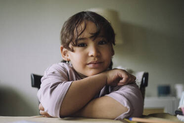 Portrait of girl leaning head on arms at table in home - MASF43230