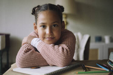 Portrait of smiling girl resting head on arms while sitting at home - MASF43233