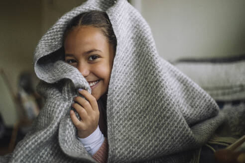 Portrait of playful girl hiding under blanket at home - MASF43243