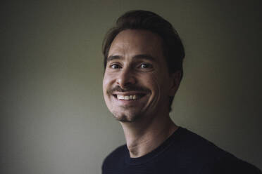 Portrait of smiling man in front of gray wall at home - MASF43248