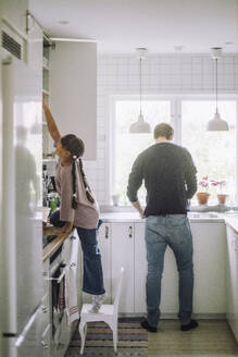 Girl reaching at cabinet with father preparing food in kitchen at home - MASF43255