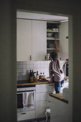 Rear view of girl reaching at cabinet in kitchen at home - MASF43257