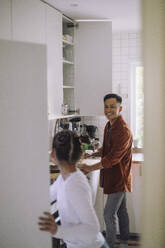 Smiling father talking to daughter while preparing food in kitchen at home - MASF43260