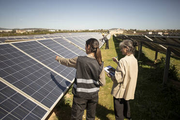 Female engineer showing solar panels to senior entrepreneur during visit at power station - MASF43282