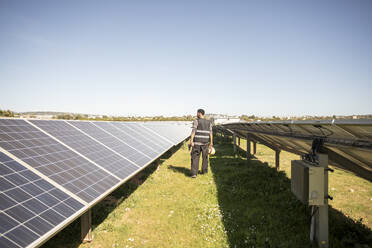 Rear view full length of male engineer examining solar panels at power station - MASF43290