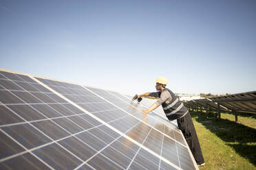 Side view of male engineer drilling on solar panels while working at power station - MASF43295