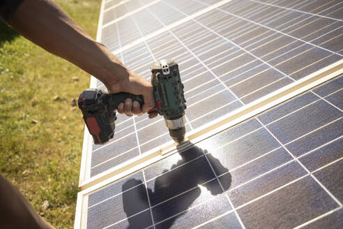 Hand of male engineer using drill on solar panels while working at power station - MASF43302