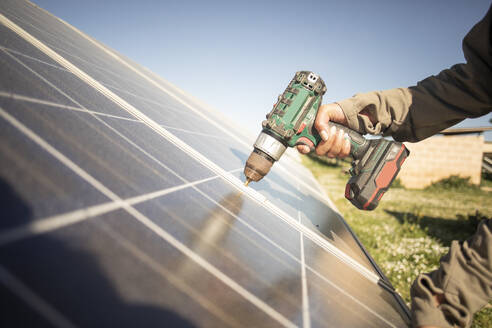 Hand of female engineer installing solar panels with drill while working at power station - MASF43314