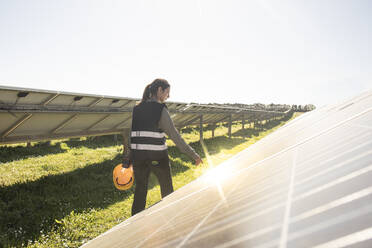 Rear view of female engineer examining solar panels at sunny day in field - MASF43316