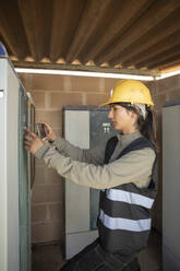 Female maintenance engineer comparing circuit board with smart phone at power station - MASF43321