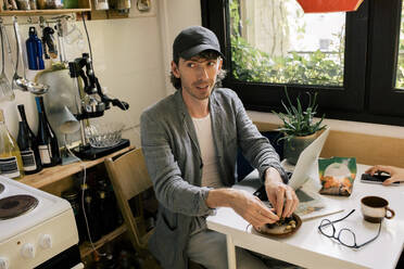 High angle view of male architect eating snacks while sitting at desk in home office - MASF43332