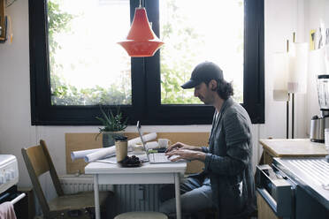 Side view of male architect using laptop at desk in home office - MASF43341