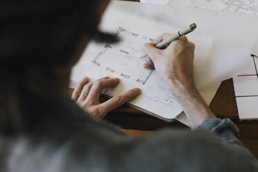 Over shoulder view of male architect sketching blueprint on paper at desk in home office - MASF43345