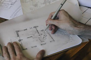 Cropped hands of male architect sketching blueprint on paper at desk in home office - MASF43346