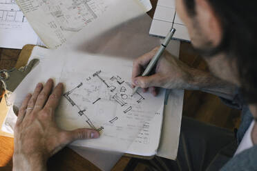 High angle view of male architect sketching blueprint on paper at desk in home office - MASF43347